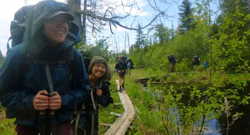 a group of outward bound students smile while hiking on an elevated wood trail through a marsh area